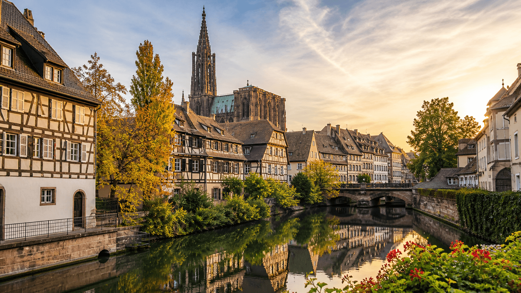 Vue panoramique de Strasbourg avec les maisons à colombages de la Petite France au bord de l’Ill et la cathédrale Notre-Dame en arrière-plan, sous une lumière dorée de fin d’après-midi.