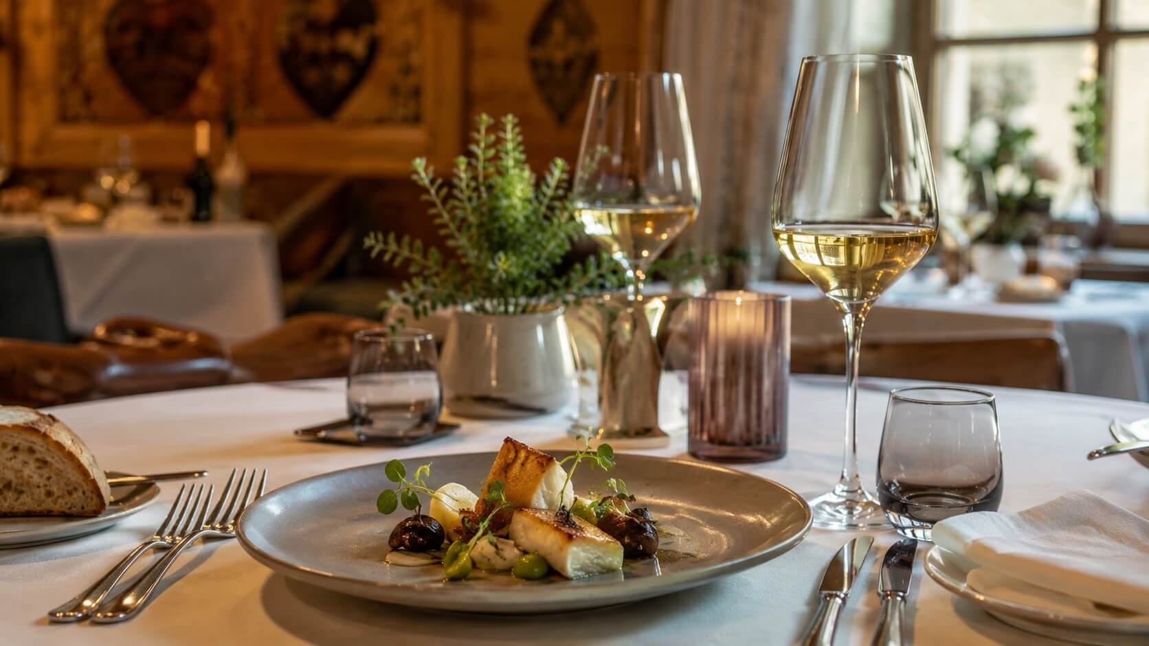 Salle élégante d’un restaurant gastronomique alsacien avec assiette raffinée, verres de vin blanc d’Alsace et ambiance chaleureuse.