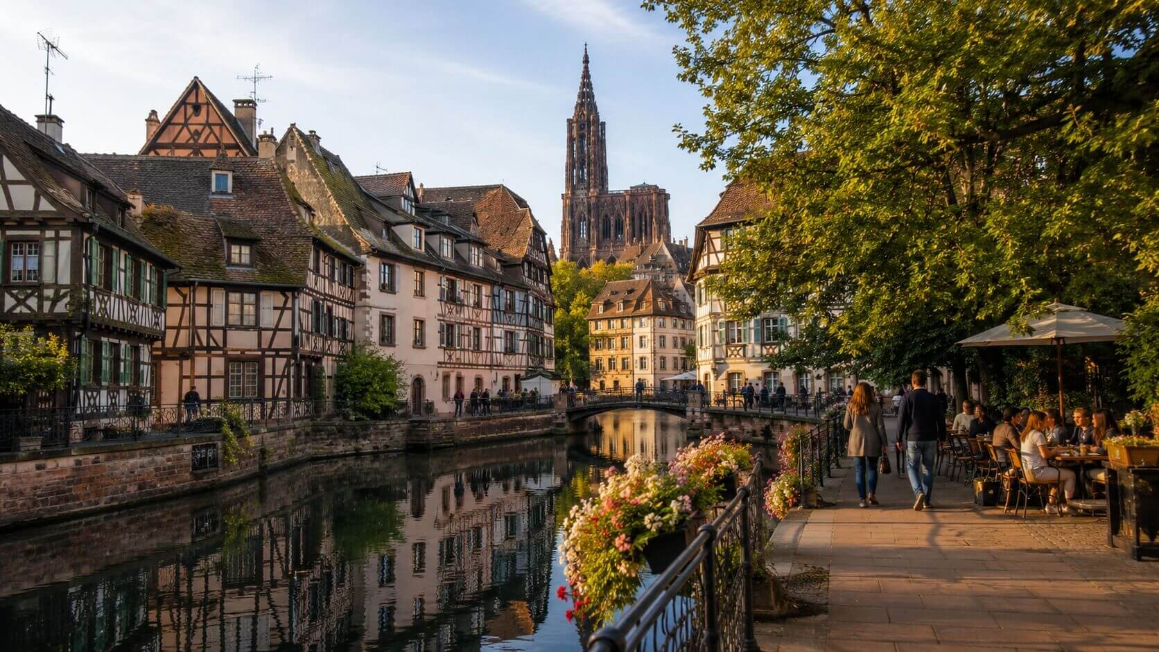 Photo réaliste en format paysage 16:9 montrant Strasbourg lors d’un week-end de visite, ambiance élégante de guide touristique, avec la cathédrale Notre-Dame en grès rose visible au loin, les maisons à colombages de la Petite France au bord de l’Ill, reflets dans les canaux, passants discrets, terrasse de winstub chaleureuse en arrière-plan, lumière douce de fin d’après-midi, atmosphère patrimoniale franco-allemande, rendu éditorial professionnel, couleurs naturelles, haute définition, sans texte, sans logo, sans watermark.