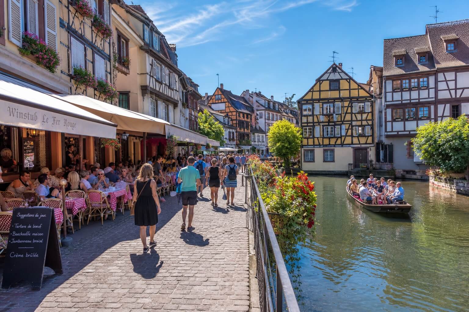 Touristes profitant des rues animées et des canaux de Colmar avec maisons à colombages et terrasses de café