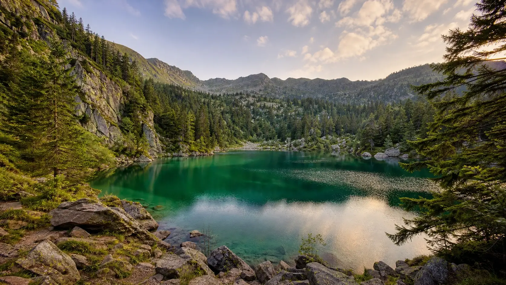 Vue du Lac Vert dans les Vosges avec son eau émeraude entourée de forêt et de rochers dans un cirque glaciaire