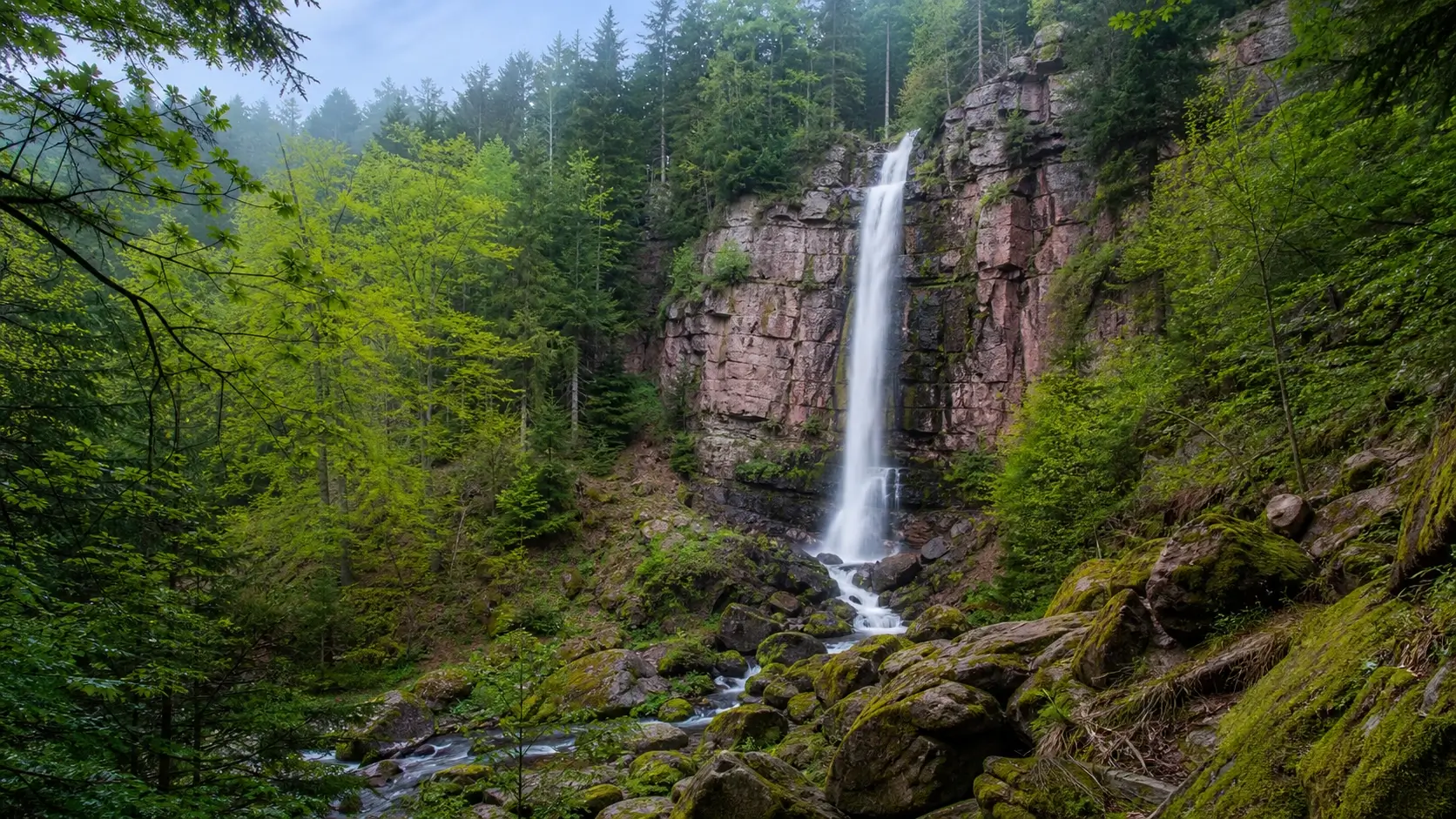 Cascade du Nideck entourée de forêt dans les Vosges du Nord avec chute d’eau sur falaise de grès rose
