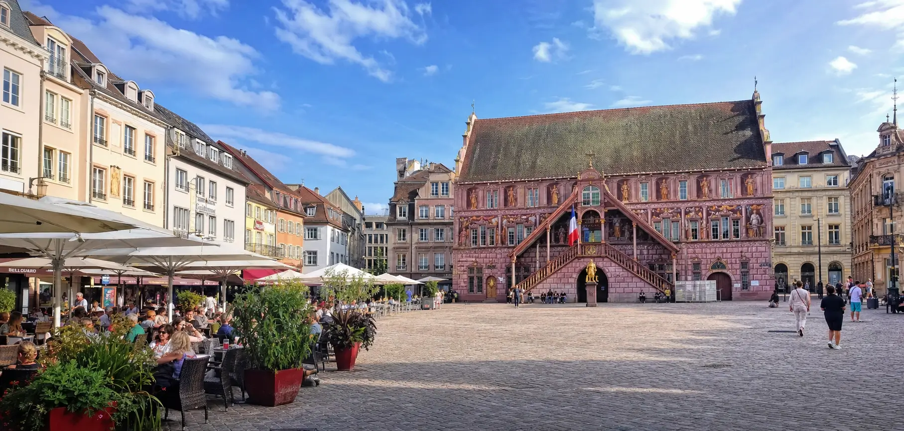 Vue de la place de la Réunion à Mulhouse avec l’hôtel de ville coloré et des terrasses animées en été
