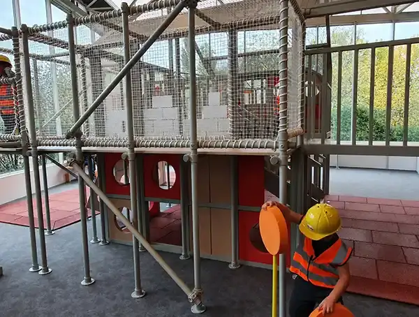 Un enfant portant un casque jaune et un gilet orange joue sur une structure d’escalade intérieure au Vaisseau à Strasbourg, en 2023.