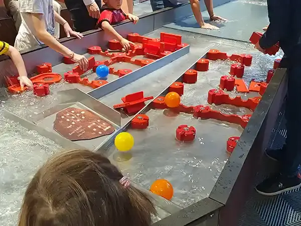 Des enfants manipulent un parcours de jeu d’eau avec des pièces rouges et des balles colorées au Vaisseau à Strasbourg, en 2023.