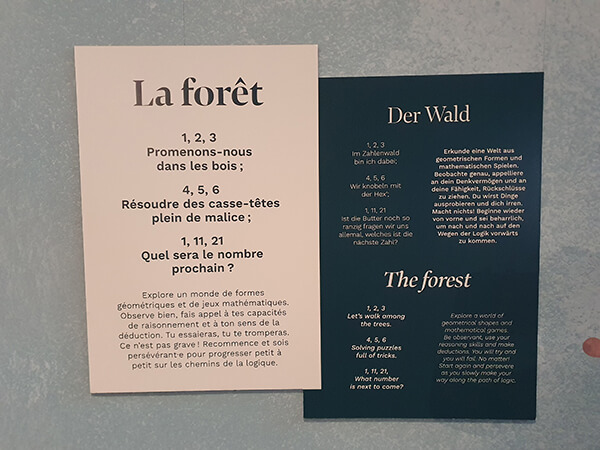 Panneaux en français, allemand et anglais présentant l’exposition « La forêt » et proposant des énigmes mathématiques, photographiés au Vaisseau à Strasbourg en 2023.